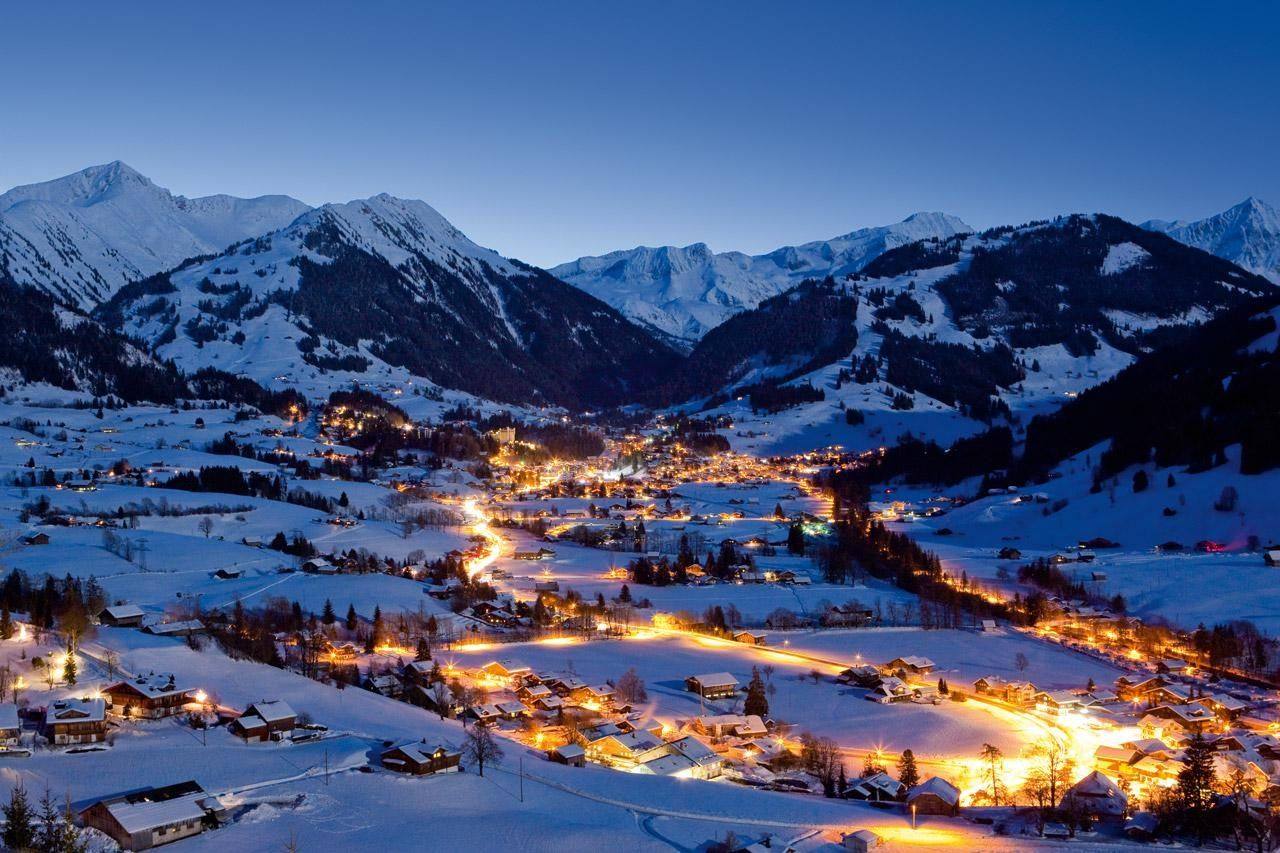 Gstaad bei Nacht — Panoramablick von der Wispile auf das beleuchtete Dorf mit verschneiten Bergen